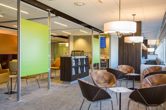 The Escape Lounge at Minneapolis-Saint Paul International Airport features a seating area with tables, chairs, and a magazine rack.