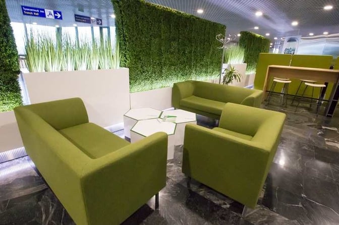 Seating area in the International Business Lounge at Minsk National Airport features comfortable chairs and tables with privacy-enhancing greenery dividers.