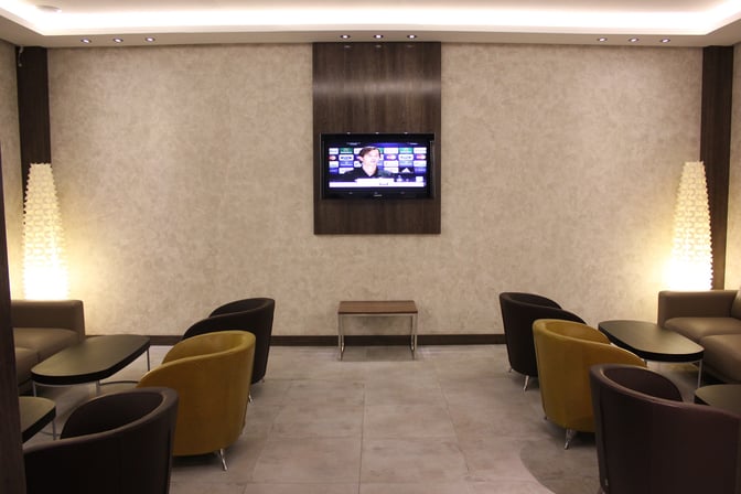 The seating area in the Primeclass Lounge at Monastir Habib Bourguiba International Airport features armchairs and a wall-mounted TV for entertainment.