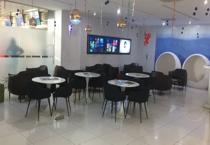 The seating area in the First Lounge at Murtala Muhammed International Airport features round tables, chairs, and digital screens for entertainment.