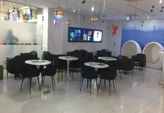 The seating area in the First Lounge at Murtala Muhammed International Airport features round tables, chairs, and digital screens for entertainment.