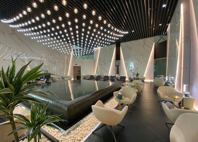 The Majan Lounge at Muscat International Airport features a seating area with armchairs and tables surrounding a central water feature.
