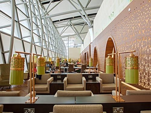 The Primeclass Lounge at Muscat International Airport features comfortable seating with individual tables and power outlets, set along a large windowed wall.