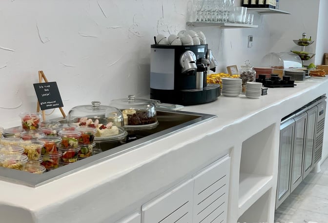 Self-serve food station at Mykonos Island National Airport lounge offers salads, desserts, and a coffee machine for travelers.