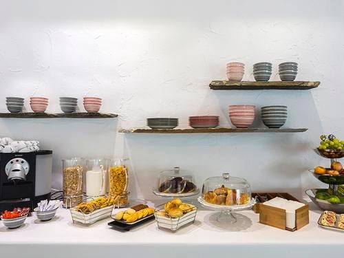 Self-serve snack station at Mykonos Island National Airport lounge offers pastries, cereals, and fresh fruit with beverage options.