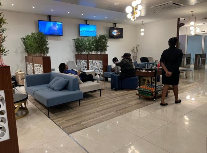 The seating area in Le Meilleur VIP Lounge at N'Djili International Airport features comfortable sofas, a refreshment cart, and multiple televisions.