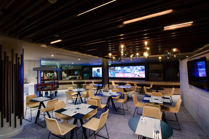 The Fiji Airways Premier Lounge at Nadi International Airport features a dining area with table seating and a large television screen.