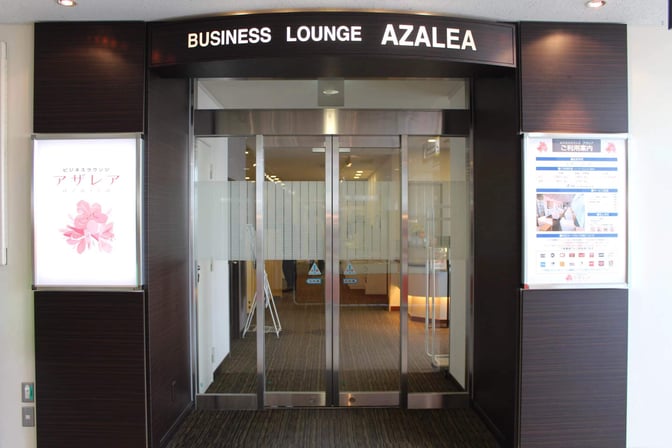The entrance to Business Lounge AZALEA at Nagasaki Airport features sliding glass doors and signage with lounge information.