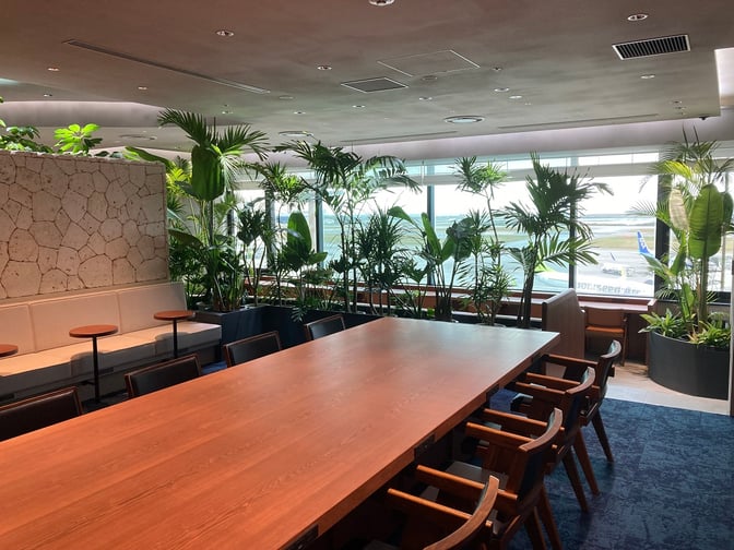 The seating area at Lounge Hana in Naha Airport features a large communal table and booth seating with views of the runway.