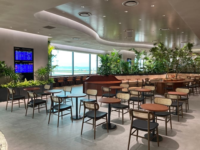 The seating area at Lounge Hana in Naha Airport features tables and chairs with views of the runway through large windows.