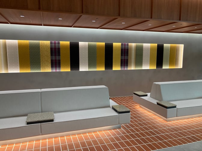 Seating area at Lounge Hana in Naha Airport features cushioned benches with integrated tables, set against a patterned wall display.