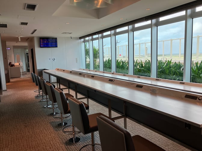 The seating area at Lounge RYURIN in Naha Airport features counter seating with power outlets and views of the runway.