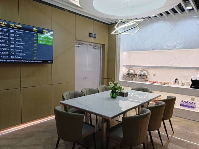 The dining area in China Southern Airlines Lounge at Nanjing Lukou Airport features a table with seating and a self-serve food station.