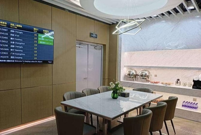 The lounge at Nanjing Lukou International Airport features a dining area with a table, seating, and a self-serve food station.