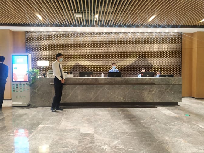 The reception area of V9 Business Lounge at Nanjing Lukou International Airport features a staffed check-in counter with digital displays.