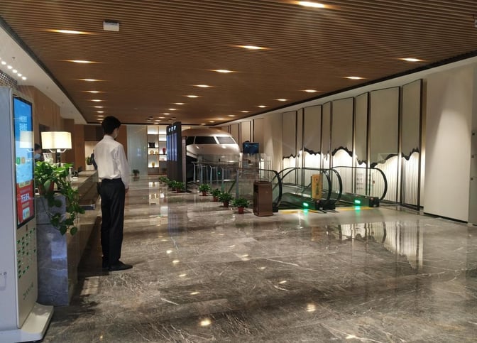 The V9 Business Lounge entrance at Nanjing Lukou International Airport features an escalator and a reception area with staff assistance.