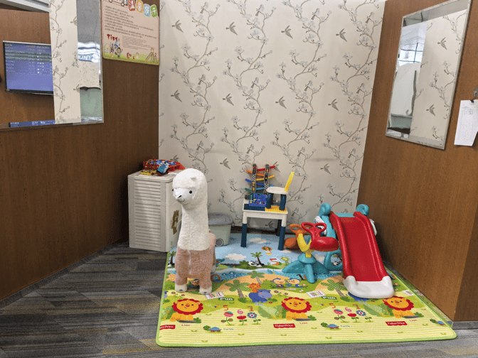 The children's play area in the V7 International First Class Lounge features toys, a small slide, and a colorful play mat.