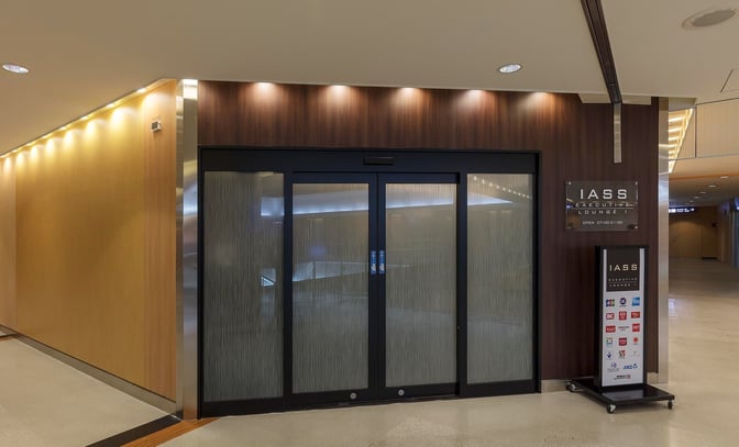 The entrance to IASS Executive Lounge 1 at Narita International Airport features sliding glass doors and signage displaying operating hours.