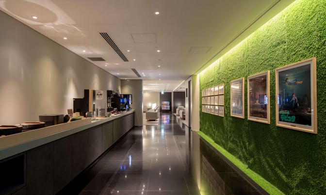 The IASS Superior Lounge at Narita International Airport features a self-serve beverage station and seating area along a corridor with framed artwork.