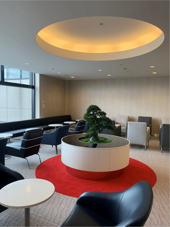 The Aspire Lounge at Narita International Airport features a seating area with armchairs and tables, centered around a decorative plant display.