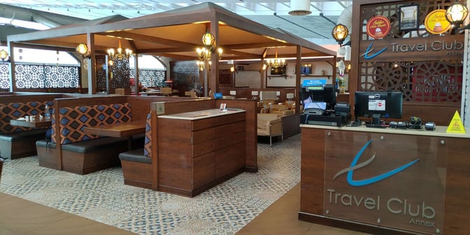 The Travel Club Annex at Kolkata Airport features a reception desk and booth seating for travelers, providing a comfortable waiting area.