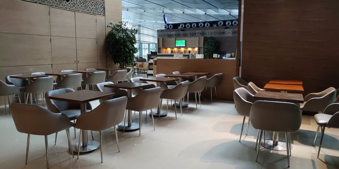 The seating area at Kolkata's Travel Club Lounge features multiple tables and chairs, with a view of the bar in the background.