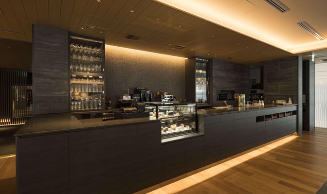 The Café Sky Library at New Chitose Airport features a counter with a display of pastries and a selection of glassware.