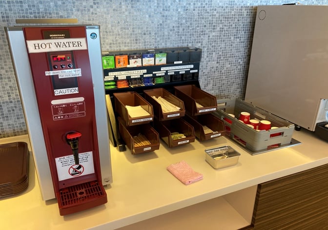 The beverage station at North Lounge, New Chitose Airport, features a hot water dispenser, tea bags, and various condiments.
