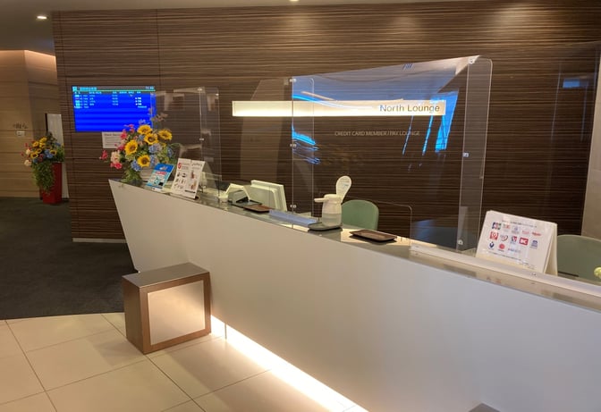The reception area of North Lounge at New Chitose Airport features a check-in counter with informational displays and floral arrangements.