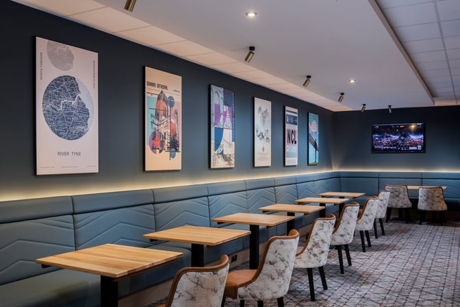 Booth seating in the Aspire Lounge at Newcastle Airport features individual tables and wall art, providing a comfortable dining area.