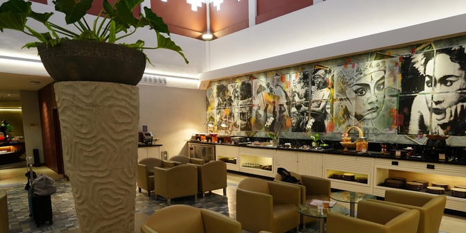 The Concordia Lounge at Ngurah Rai International Airport features a seating area with armchairs and a buffet counter with snacks.