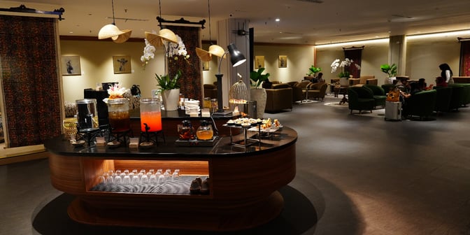 The Concordia Lounge at Ngurah Rai International Airport features a self-serve beverage and snack station with comfortable seating areas nearby.