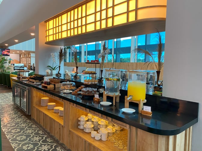 The Concordia Lounge at Ngurah Rai International Airport features a self-serve beverage and snack station with various refreshments and cups.