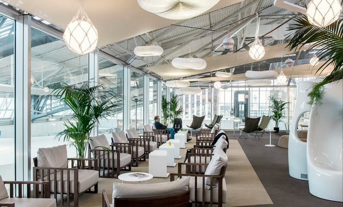 The Canopy Lounge at Nice International Airport features comfortable seating with armchairs and tables, offering views of the terminal through large windows.