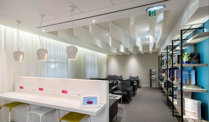 The Library Lounge at Nice International Airport features a seating area with armchairs, a work counter with charging ports, and bookshelves.
