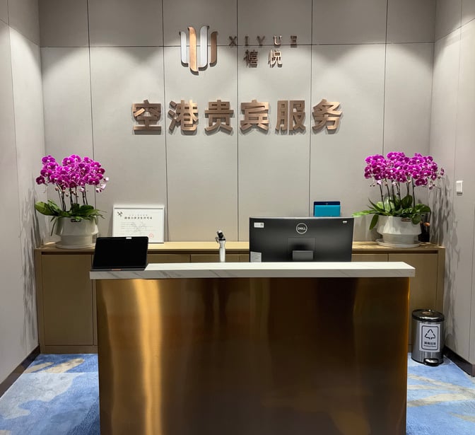 The reception area at Ningbo Lishe International Airport's First Class Lounge 2 features a service desk with computer and decorative plants.