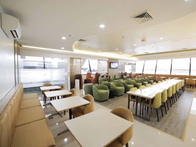 The Marhaba Lounge at Ninoy Aquino International Airport features a spacious seating area with tables, chairs, and airport views.