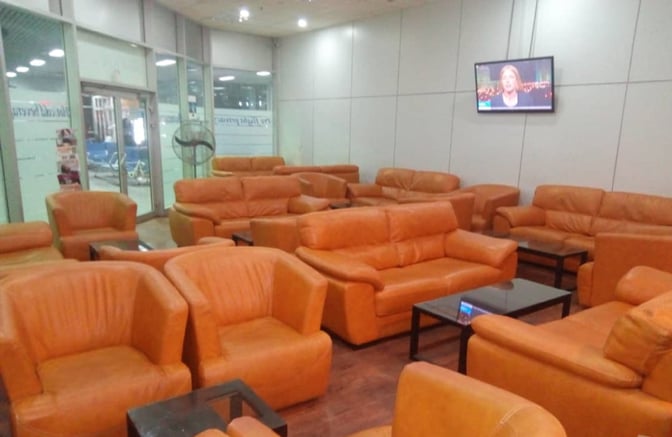 The seating area in Lounge One at Nnamdi Azikiwe International Airport features multiple sofas and armchairs with a wall-mounted TV.