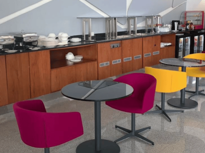 The Pearl Lounge at Nnamdi Azikiwe International Airport features a self-serve food area with tables and colorful seating.