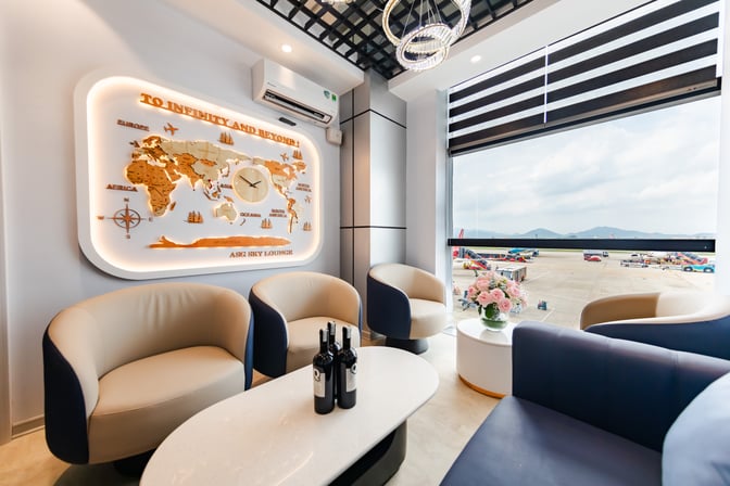 Seating area in ASG Sky Lounge at Noi Bai International Airport features comfortable chairs, a table with wine, and a view of the tarmac.