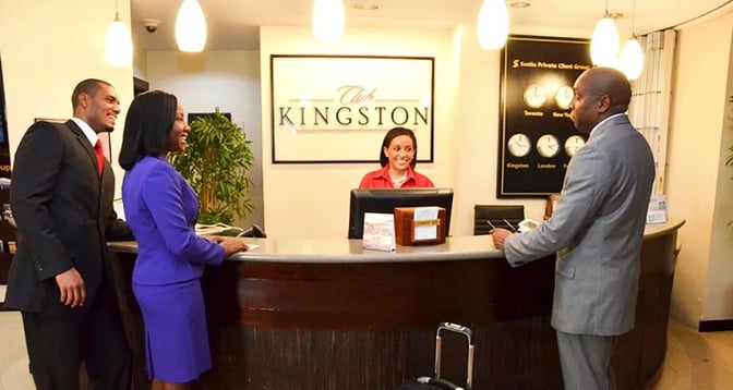 The reception desk at Club Kingston in Norman Manley International Airport features staff assisting travelers with lounge access inquiries.