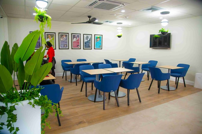 The seating area in Club Kingston at Norman Manley International Airport features tables and chairs with framed artwork on the walls.