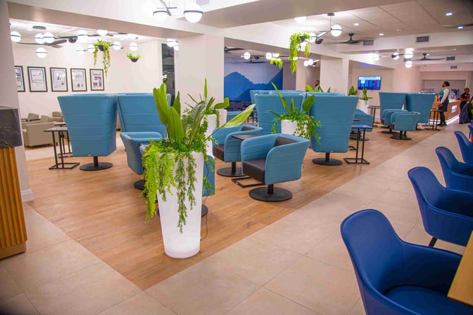 The seating area in Club Kingston at Norman Manley International Airport features swivel chairs and tables, with decorative plants throughout.