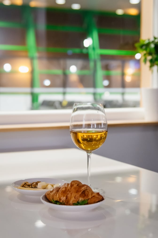 A table at Sapar Lounge in Nursultan Nazarbayev International Airport features a glass of wine and plates with snacks.