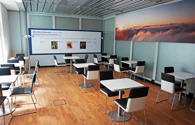 The Durer Lounge at Nuremberg Airport features a seating area with tables and chairs, accompanied by informational wall displays.