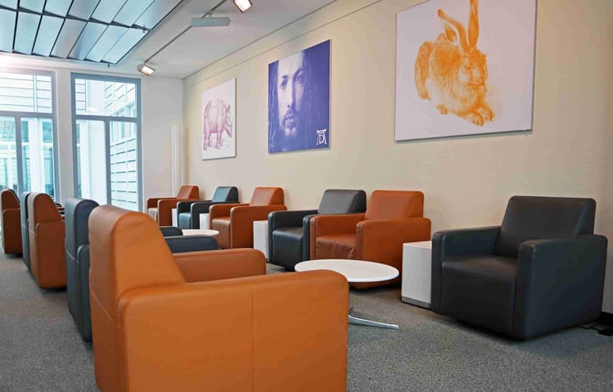 The Durer Lounge at Nuremberg Airport features comfortable armchairs and small tables, with artwork displayed on the walls.