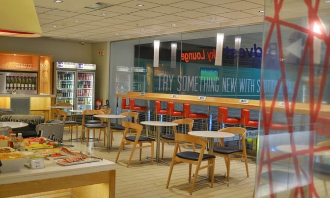 The Bidvest Sky Lounge at O. R. Tambo International Airport features a self-serve food station and seating area with tables and chairs.
