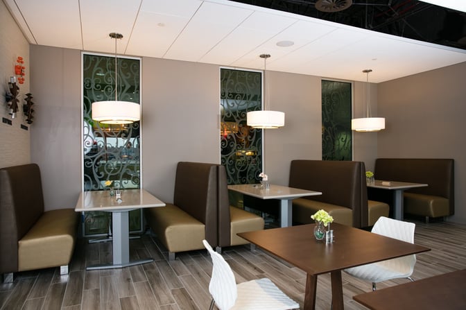 Booth seating in the Escape Lounge at Oakland International Airport offers semi-private dining areas with decorative partitions and overhead lighting.