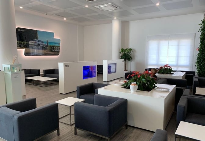 The Olbia Airport Club Lounge features seating areas with tables and plants, providing a comfortable space for travelers to relax.