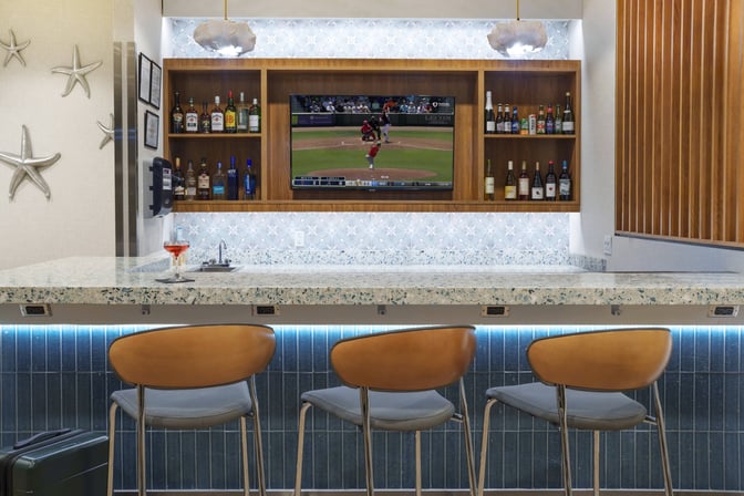 The bar at Club MCO Airside 1 features a variety of spirits and a television, with seating available for guests.